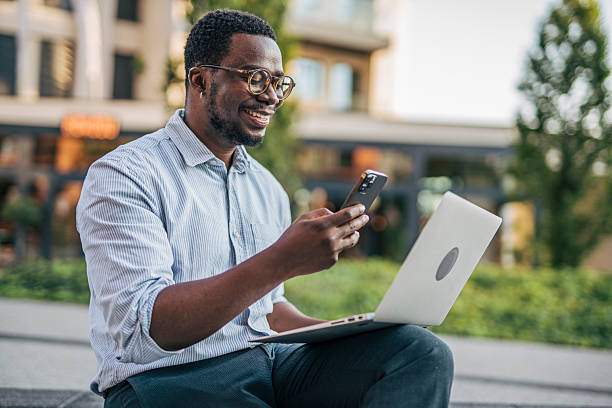 istock Smiling businessman using laptop and smartphone outdoors 2230416817
