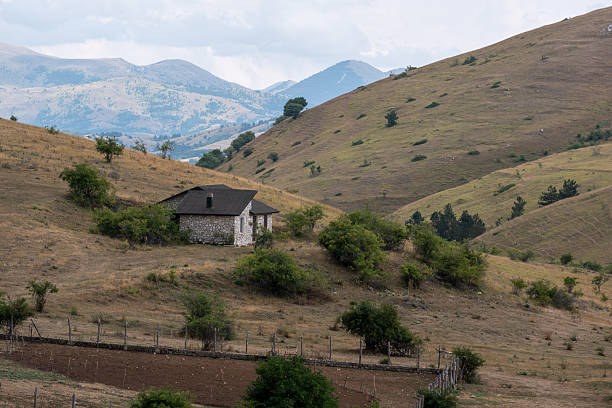 A serene view of a country house surrounded by leafless trees, hills, and partially snow-covered ground on a sunny late winter day showcasing rural tranquillity.