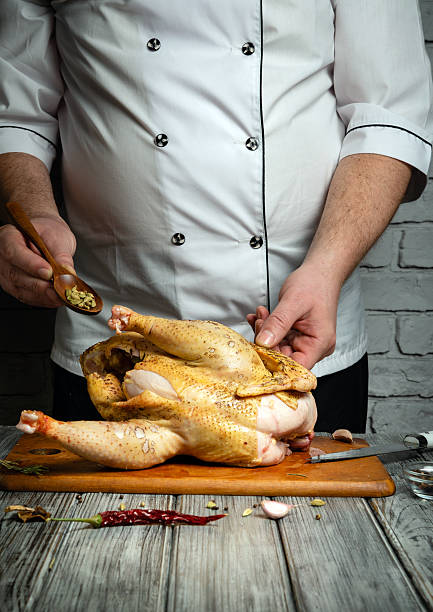 istock A chef skillfully seasons a whole chicken with herbs and spices in a cozy kitchen. The rustic atmosphere features wooden surfaces and brick walls, enhancing the culinary experience 2230421250