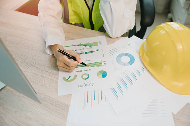 istock Business analysis with charts and graphs by engineer in safety vest with hard hat working on project data in modern office 2230423075