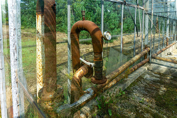 Rusty pipes and heating system valves inside an abandoned greenhouse, with visible pressure gauge and glass, symbolizing decay, corrosion, and the deterioration of old industrial infrastructure.