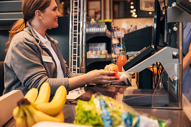 istock Side view of a female smiling cashier using barcode scanner on a pack on spaghetti, focus on her hands 2230433992