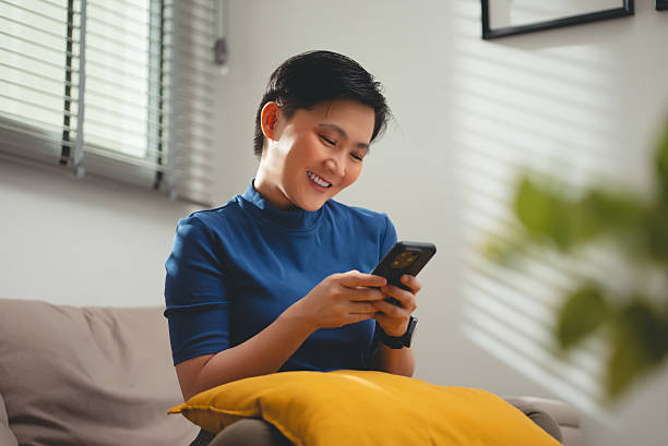 istock Asian woman happy smiling sitting on sofa and using smart phone at home. 2230438076