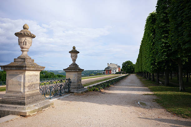 Stone balustrade with decorative urns and garden pathway lined by green trees in Saint Germain France