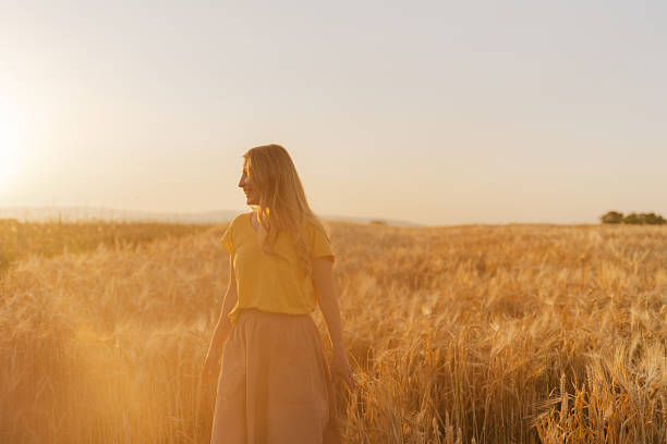 Portrait of a mid-adult woman with a golden hair, standing outdoors in a golden wheat field
