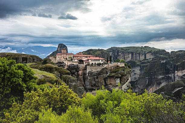 Panoramic view of a Meteora monastery perched on a steep rock formation in central Greece, UNESCO World Heritage Site, under dramatic cloudy sky.