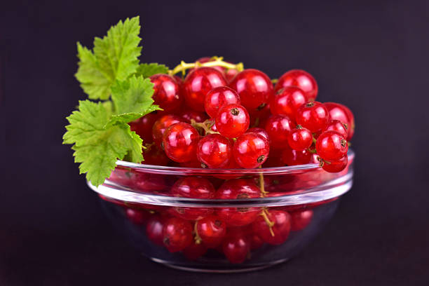 Red currant berries in a glass bowl on a black background. Close-up.