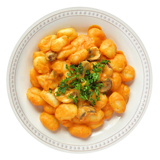 A close-up of a bowl of gnocchi covered in rich tomato sauce and topped with freshly grated cheese. The dish is served in a ceramic bowl on a neutral tablecloth, with a fork and drink visible softly in the background. Warm colors and soft lighting evoke a comforting homemade meal, ideal for themes related to Italian cuisine, comfort food, pasta dishes and cozy home dining.