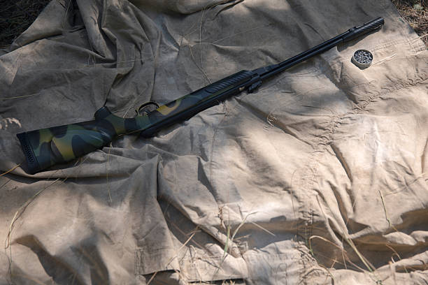 Camouflaged air rifle with pellets resting on a canvas sheet in the woods, ready for hunting or target practice