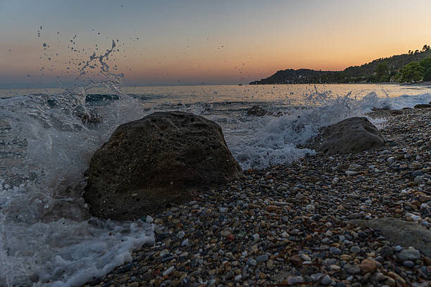 A serene view of waves splashing against rugged rocks, capturing the tranquil essence of a sunset at the beach, with soft colors blending in the sky and water.
