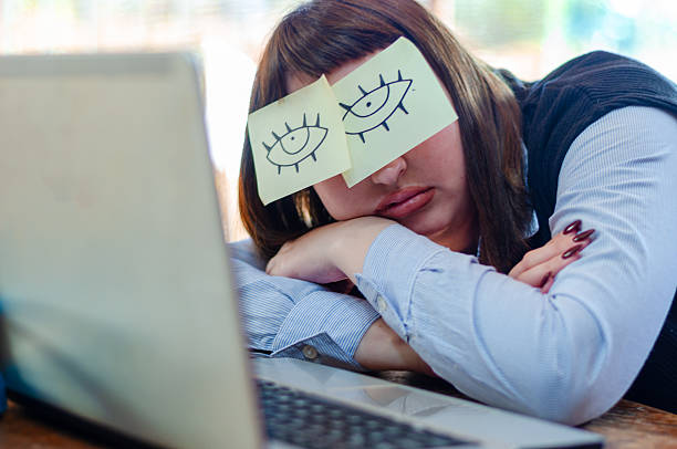 Lazy unproductive young guy wearing funny sticky notes with open eyes on his glasses, sleeping at workplace