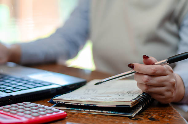 istock Close up of a hands of a young woman taking notes on a note pad while working with a laptop 2230457121