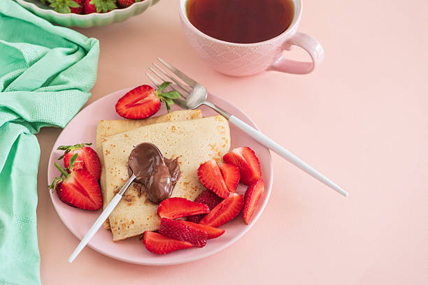 Crepes with chocolate spread and fresh strawberries, served with tea on pink background