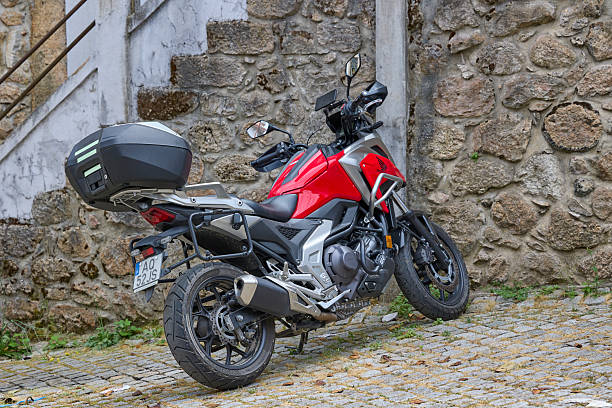 Red motorcycle parked on cobblestone street near stone wall. Piodao, Portugal - June 21, 2025.