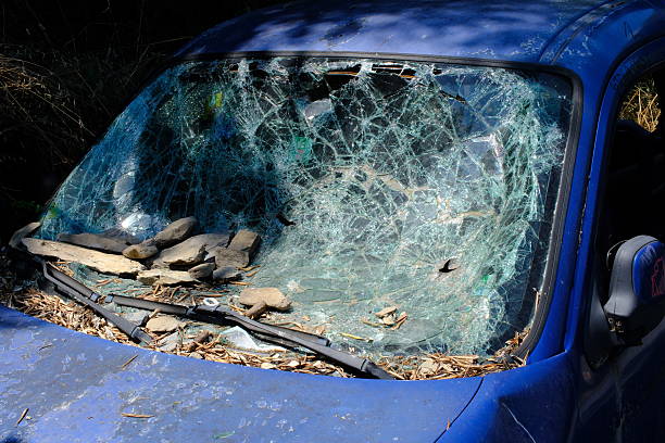 A white car is left abandoned with missing parts and covered in dust. It rests on stones in a quiet neighborhood. Evening light creates a serene atmosphere around the scene.