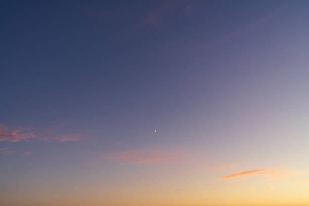 Serene twilight sky with a beautiful color gradient from orange to blue, featuring a waxing crescent moon and clouds.High quality photo