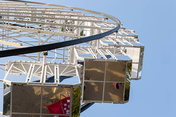 Ferris wheel gondolas reflecting blue sky and ground below on a sunny day