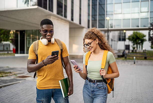 istock Smiling students walking and using smartphones outdoors 2230499509