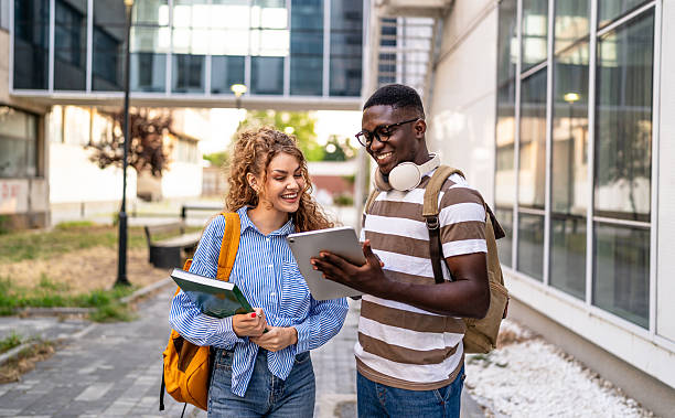istock Cheerful students walking and using digital tablet outdoors 2230499613