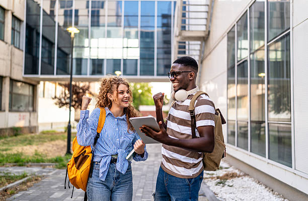 istock Happy students celebrating success outdoors with digital tablet 2230499628