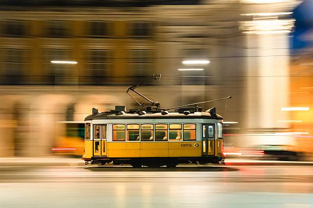 A vintage yellow tram in motion blurs through Lisbon's cityscape at night, capturing urban transit energy.