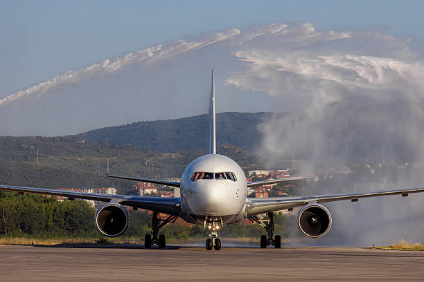 Welcoming the arriving aircraft with a water cannon down the runway under blue sky with mountains and clouds emerging in the background.
