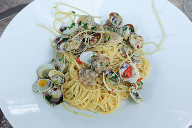 A plate of seafood pasta. A wedge of parmesan cheese and a cluster of basil sit next to the dish.