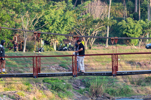 Payakumbuh, Indonesia, June 29, 2025: People walking on suspension bridge over river in tropical nature, outdoor travel adventure and rural lifestyle concept.