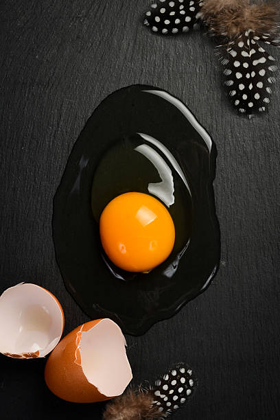istock Close-up of a raw chicken egg broken on a slate surface. On a black stone background. Top view. 2230538769