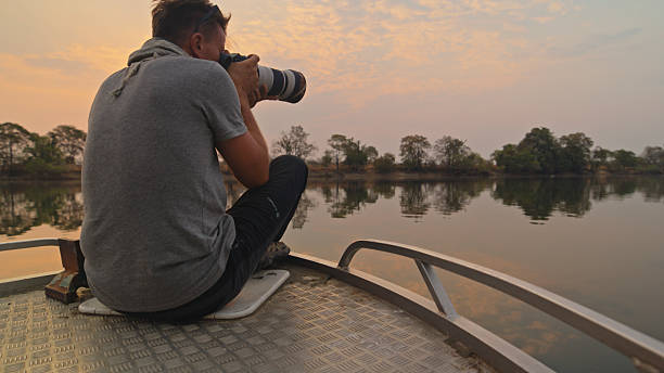 istock Photographer on Boat Capturing Tranquil River Scene at Sunset 2230541726