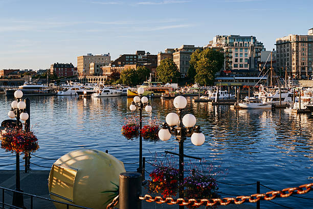 A dock and waterfront walkway with flower decorations and boats in the harbor at sunset in Victoria, Vancouver Island, Canada.