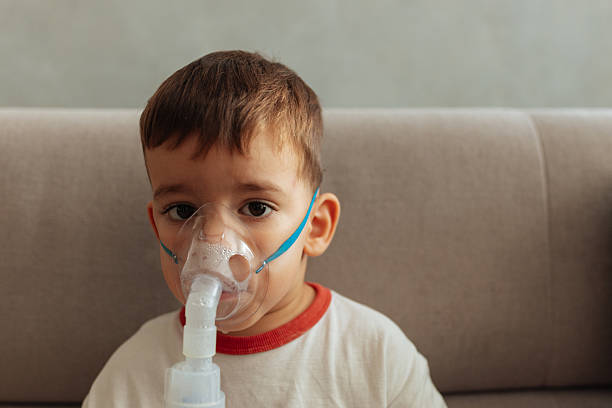 istock Little boy using a medical nebulizer mask at home 2230554713