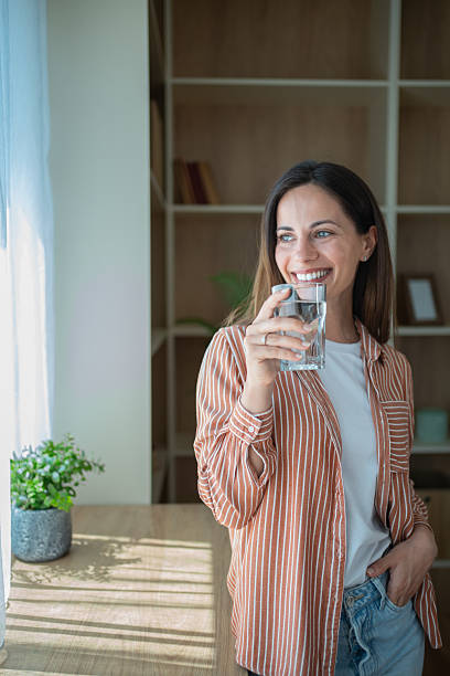 istock Young woman drinking water and smiling by the window 2230558017