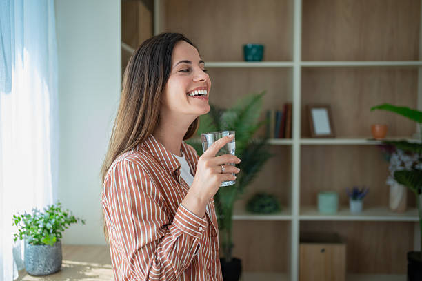 istock Young woman laughing while drinking water at home 2230558071