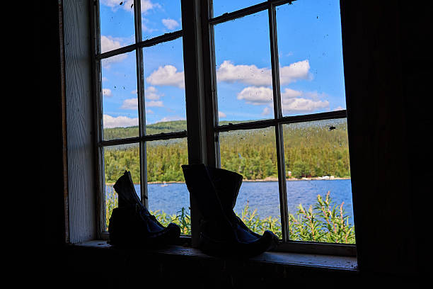 old boots standing in a window of a typical swedish log hut or cabin in the woods surrounded by tall pine trees in the dense forests of scandinavia.