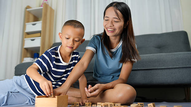Mother and son are engaged in playful activity, building with wooden blocks on soft surface. room is bright and inviting, showcasing cozy atmosphere filled with joy and learning