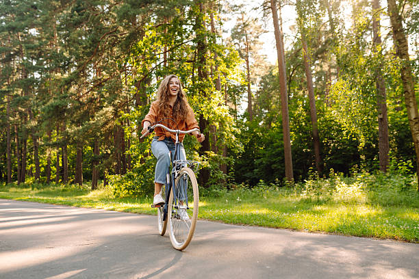 istock Young woman riding a bicycle on a path in a dense sunny forest. 2230573283