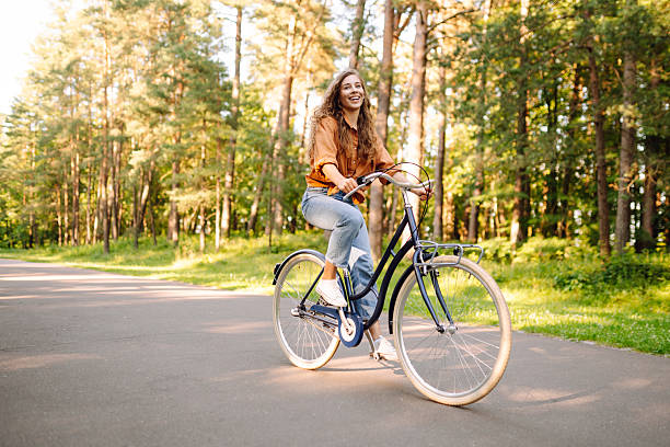 istock Young woman riding a bicycle on a path in a dense sunny forest. 2230573306