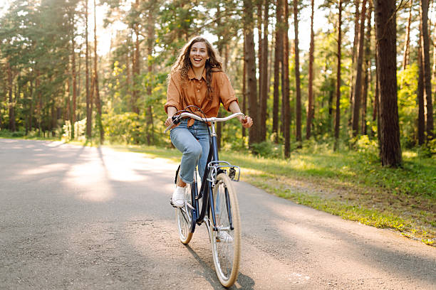 istock Young woman riding a bicycle on a path in a dense sunny forest. 2230573425