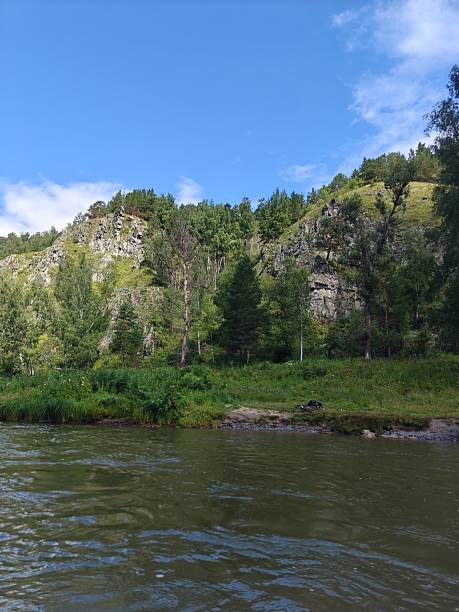 istock Serene River Landscape with Lush Greenery and Rocky Cliffs Under Blue Sky 2230574134