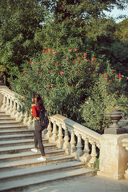 Young girl with backpack outdoors. Happy woman dressed in casual clothes walking in a city park. Holidays and tourism concept.