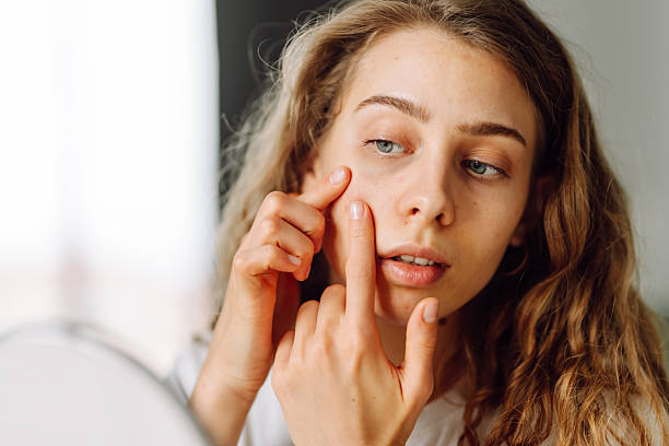 istock Curly woman examines her skin and touches it with hands while looking into small mirror. 2230577107