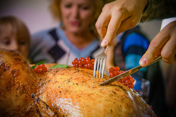 Close-up of hands carving a golden roasted turkey served with red berries, while family members gather around the festive table. Warm and inviting holiday atmosphere, perfect for Thanksgiving, Christmas, or family gatherings. Symbol of tradition, togetherness, and celebration with homemade food.