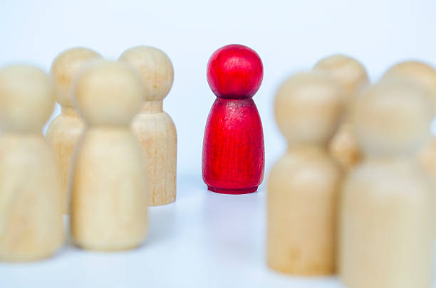 istock A single red figure stands apart from grouped wooden figures, symbolizing exclusion and discrimination concept 2230580474