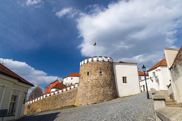 Cobblestone street leading to the historic Putimska Gate Tower in Pisek, Czechia, under a blue sky with white clouds