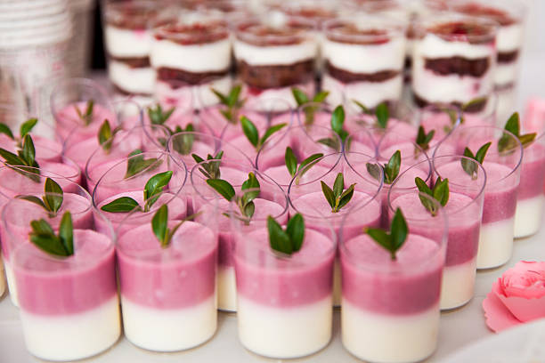 Assortment of layered mousse desserts in cups, with pink and white cream, decorated with green leaves on top.