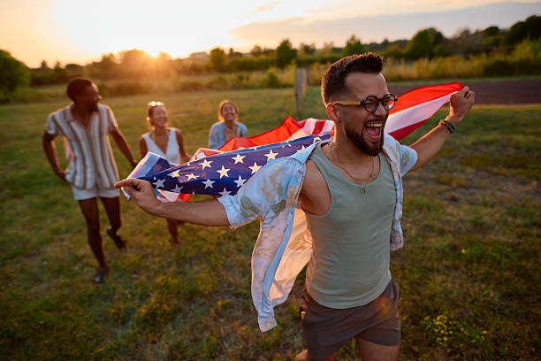 istock Young man running with american flag at sunset with friends 2230592802