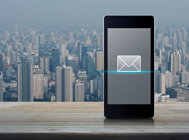 email flat icon on modern smart mobile phone screen on wooden table over city tower and skyscraper, Business communication online concept