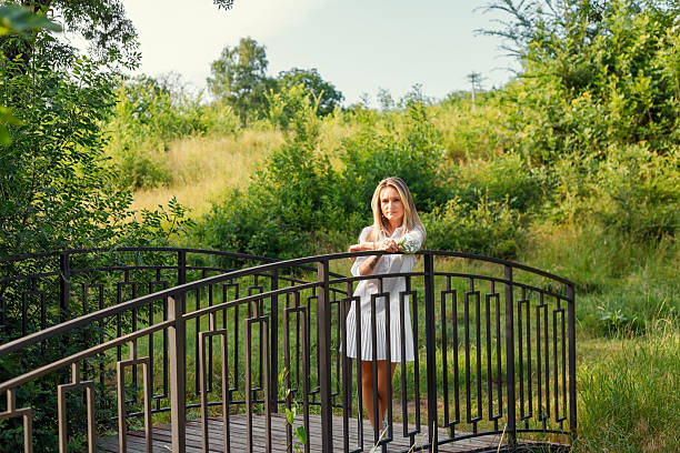 Young blonde woman relaxing on a bridge in a park during a sunny summer day