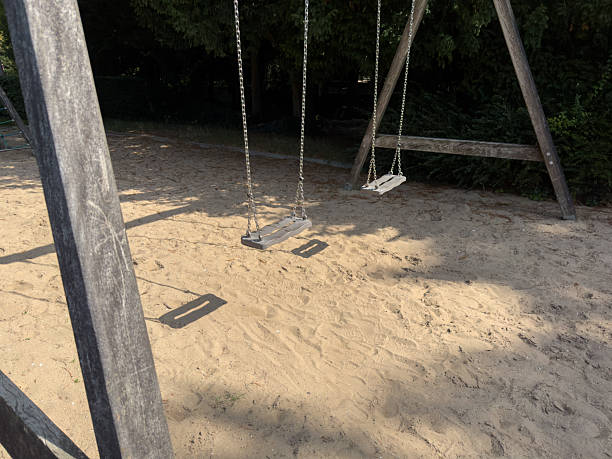 istock Empty swings on a playground surrounded by sandy ground and trees, symbolizing the end of children's holidays and the return to school 2230596116